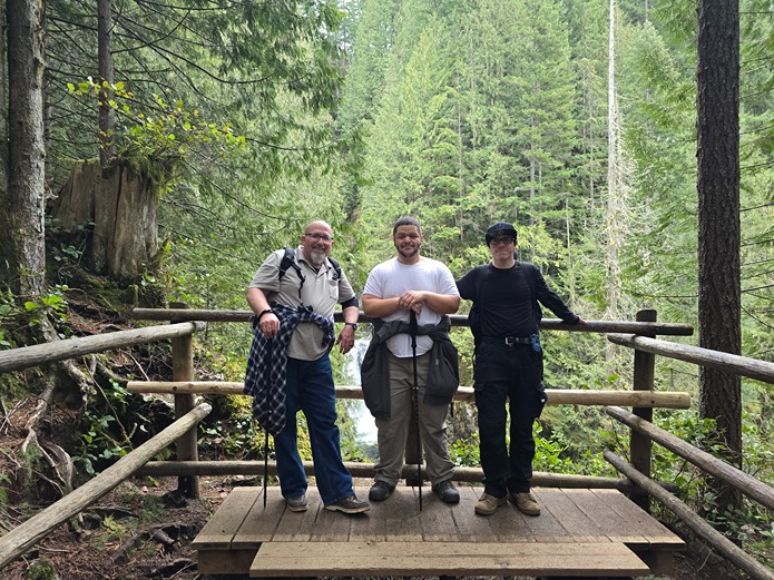 Three hikers posing on a wooden platform at the end of a trail in the forest